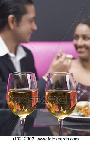 Stock Photo - Close-up of wine glasses with a mid adult man and a young woman sitting in the background. Fotosearch