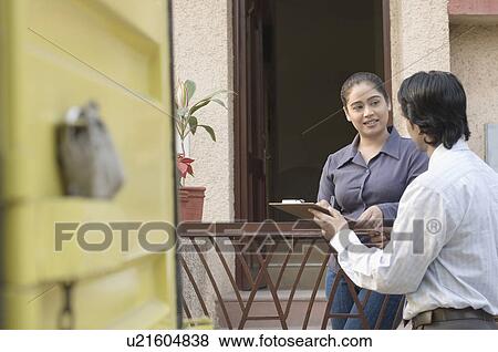 Stock Photo - Delivery man and a young woman holding a clipboard and talking to each other. Fotosearch