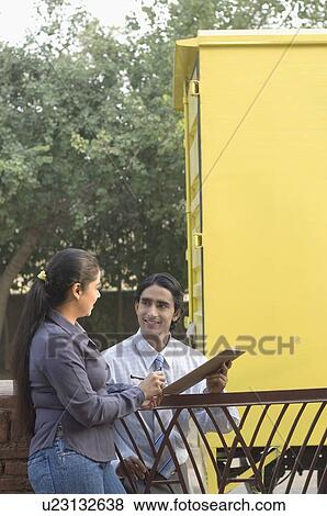 Stock Photo - Delivery man holding a clipboard and talking to a young woman. Fotosearch