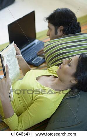 High angle view of a mid adult man using a laptop with a young woman leaning on his back and reading a book View Large Photo Image Stock Image - High angle view of a mid adult man using a laptop with a young woman leaning on his back and reading a book. Fotosearch