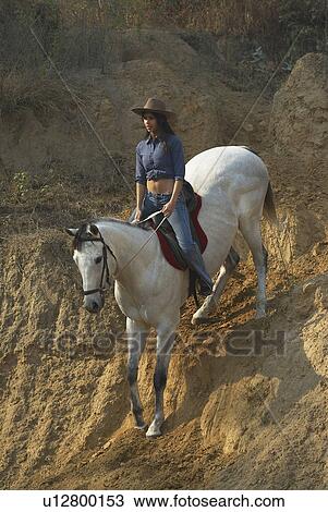 Stock Image - High angle view of a young woman riding a horse. Fotosearch