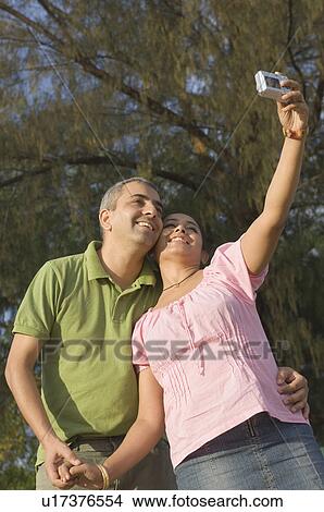 Low angle view of a mid adult couple taking a photograph of themselves and smiling View Large Photo Image Picture - Low angle view of a mid adult couple taking a photograph of themselves and smiling. Fotosearch