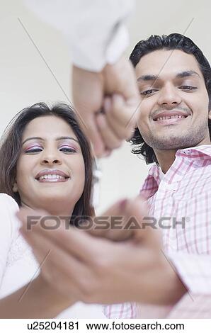 Stock Image - Low angle view of a person's hand handing over the keys to a young couple. Fotosearch