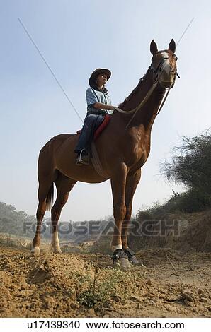 Stock Image - Low angle view of a teenage girl riding a horse. Fotosearch