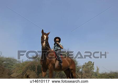 Stock Photo - Low angle view of a teenage girl riding a horse and holding a pair of binoculars. Fotosearch