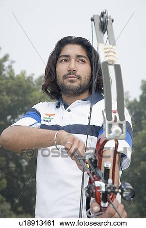 Low angle view of a young man holding a bow and arrow View Large Photo Image Stock Image - Low angle view of a young man holding a bow and arrow. Fotosearch