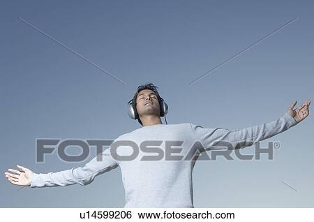 Low angle view of a young man standing with his arms outstretched and listening to music View Large Photo Image Stock Photograph - Low angle view of a young man standing with his arms outstretched and listening to music. Fotosearch