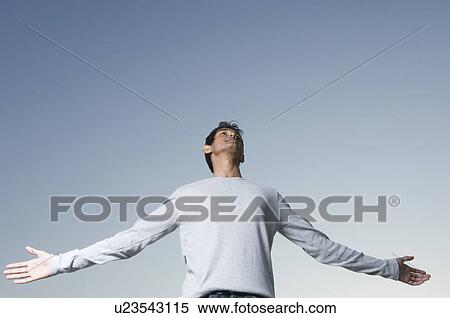 Stock Photography - Low angle view of a young man standing with his arms outstretched. Fotosearch