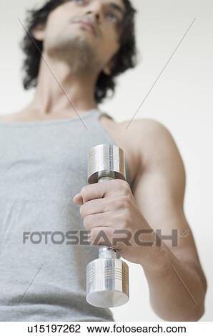 Stock Image - Low angle view of a young man exercising with a dumbbell. Fotosearch