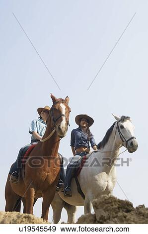 Low angle view of a young woman and a teenage girl riding horses View Large Photo Image Stock Photo - Low angle view of a young woman and a teenage girl riding horses. Fotosearch