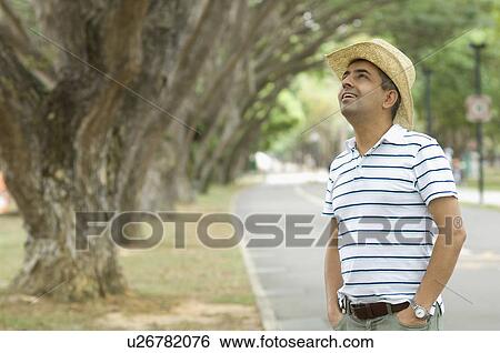 Stock Photograph - Mid adult man looking up with his hands in his pockets. Fotosearch