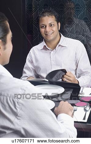 Mid adult man sitting with his friend at a table in a restaurant View Large Photo Image Stock Image - Mid adult man sitting with his friend at a table in a restaurant. Fotosearch