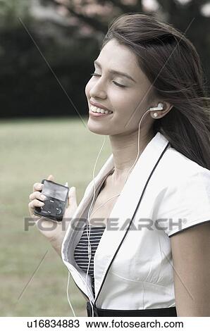 Stock Image - Mid adult woman listening to an MP3 player and smiling. Fotosearch
