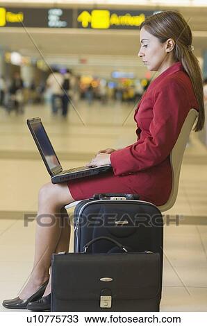 Stock Image - Mid adult woman using a laptop at an airport lounge. Fotosearch