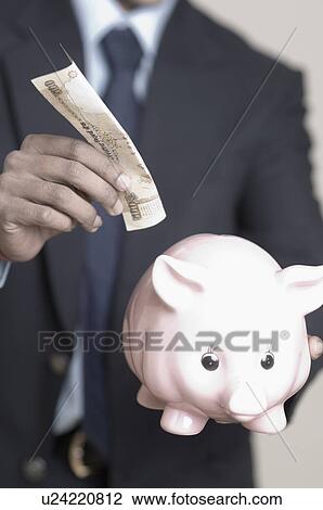 Mid section view of a businessman putting money in a piggy bank View Large Photo Image Stock Image - Mid section view of a businessman putting money in a piggy bank. Fotosearch