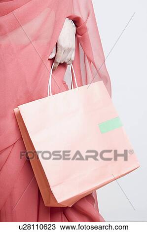 Stock Image - Mid section view of a woman holding a shopping bag. Fotosearch