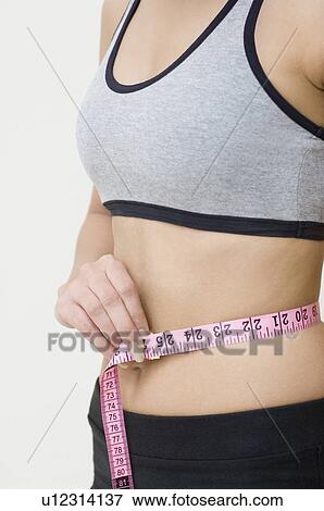 Mid section view of a woman measuring her waist with a tape measure View Large Photo Image Stock Photo - Mid section view of a woman measuring her waist with a tape measure. Fotosearch