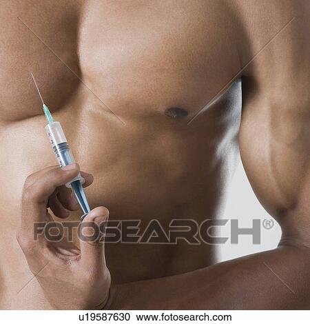 Stock Image - Mid section view of a young man holding a syringe against his chest. Fotosearch