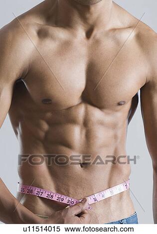 Stock Photography - Mid section view of a young man measuring his waist with a tape measure. Fotosearch
