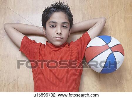 Stock Image - Portrait of a boy lying on a hardwood floor with a basketball beside him. Fotosearch