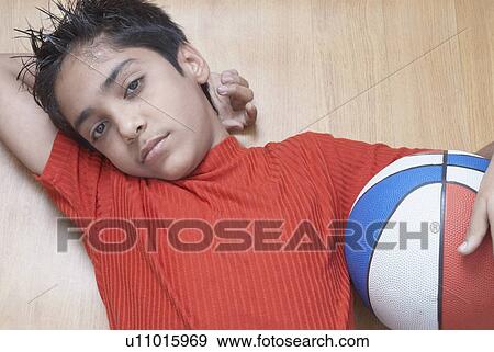 Portrait of a boy lying on a hardwood floor and holding a basketball View Large Photo Image Stock Photo - Portrait of a boy lying on a hardwood floor and holding a basketball. Fotosearch