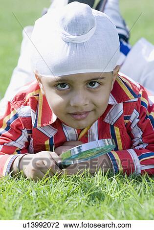 Portrait of a boy lying on grass and holding a magnifying glass View Large Photo Image Stock Image - Portrait of a boy lying on grass and holding a magnifying glass. Fotosearch