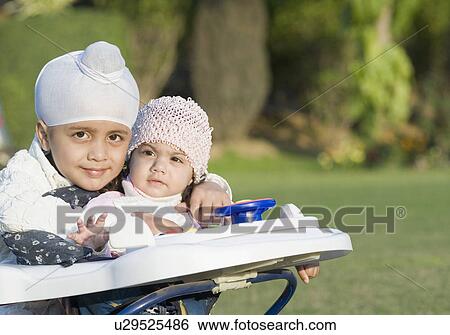 Stock Photograph - Portrait of a boy with his sister sitting in a baby walker. Fotosearch