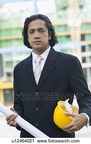 Stock Image - Portrait of a businessman holding a blueprint and a hardhat. Fotosearch