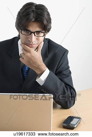 Stock Image - Portrait of a businessman sitting at a desk in front of a laptop. Fotosearch