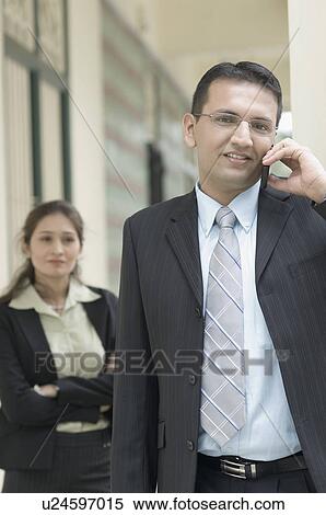 Portrait of a businessman talking on a mobile phone with a businesswoman standing behind him View Large Photo Image Stock Photography - Portrait of a businessman talking on a mobile phone with a businesswoman standing behind him. Fotosearch