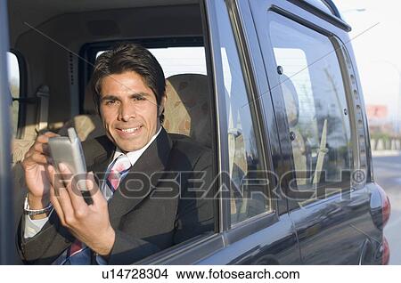 Picture - Portrait of a businessman using a personal data assistant in a car. Fotosearch