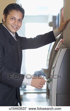 Stock Photo - Portrait of a businessman using an ATM machine. Fotosearch