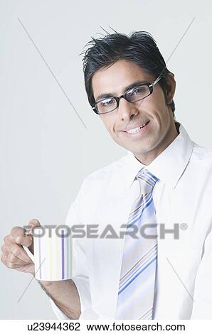 Stock Image - Portrait of a businessman wearing eyeglasses and holding a cup of coffee. Fotosearch