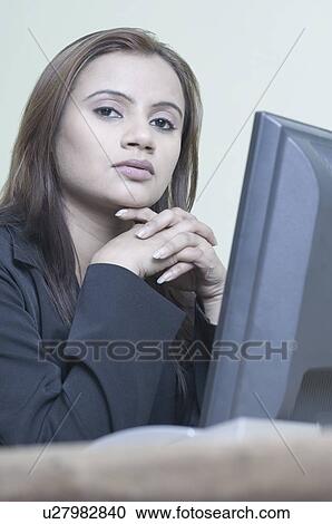 Stock Image - Portrait of a businesswoman sitting in front of a computer with her hands clasped. Fotosearch