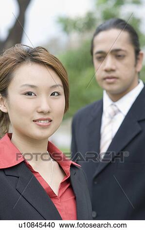 Stock Image - Portrait of a businesswoman smiling with a businessman standing beside her. Fotosearch