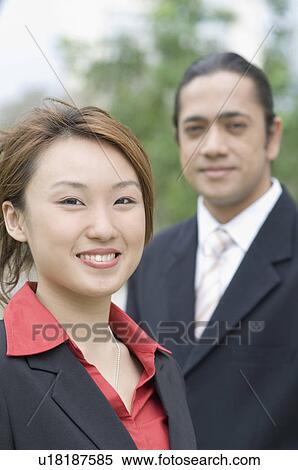 Stock Photography - Portrait of a businesswoman smiling with a businessman standing beside her. Fotosearch