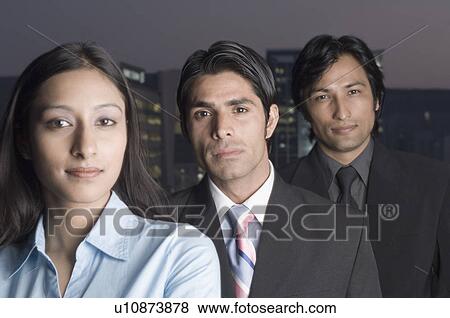 Stock Photo - Portrait of a businesswoman standing with two businessmen behind her. Fotosearch