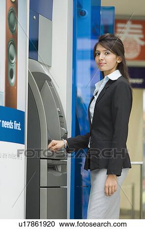 Stock Image - Portrait of a businesswoman using an ATM machine. Fotosearch