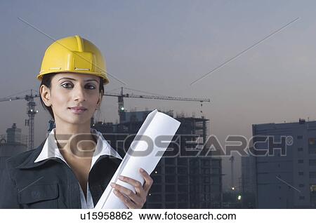 Stock Image - Portrait of a businesswoman wearing a hardhat and holding a blueprint. Fotosearch