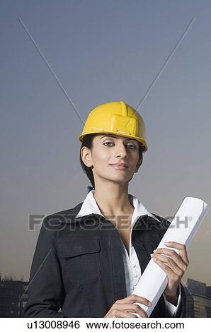 Stock Photograph - Portrait of a businesswoman wearing a hardhat and holding a blueprint. Fotosearch