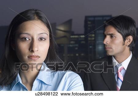 Stock Image - Portrait of a businesswoman with a businessman behind her. Fotosearch