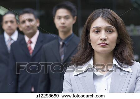 Stock Image - Portrait of a businesswoman with three businessmen standing behind her. Fotosearch