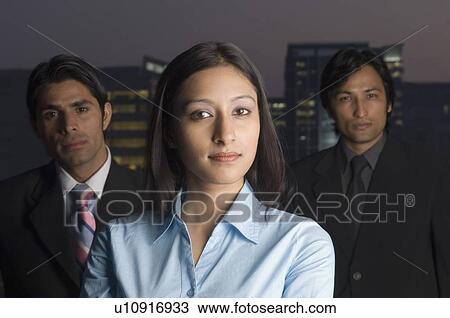 Stock Image - Portrait of a businesswoman with two businessmen standing behind her. Fotosearch