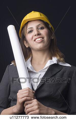 Stock Image - Portrait of a female architect holding a blueprint and smiling. Fotosearch