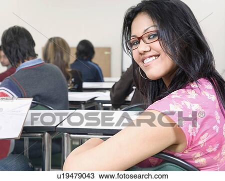 Stock Image - Portrait of a female college student sitting in an examination room and smiling. Fotosearch