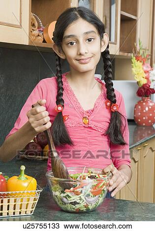 Stock Image - Portrait of a girl mixing salad with a wooden spoon. Fotosearch