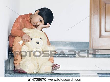 Stock Image - Portrait of a girl sitting with a teddy bear on steps. Fotosearch