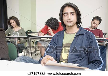 Stock Image - Portrait of a male college students giving an exam in a classroom. Fotosearch