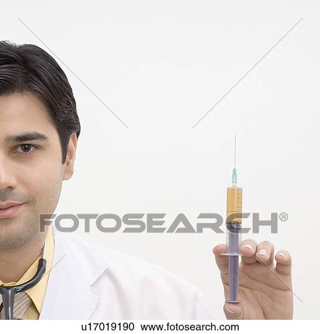 Stock Image - Portrait of a male doctor holding a syringe. Fotosearch