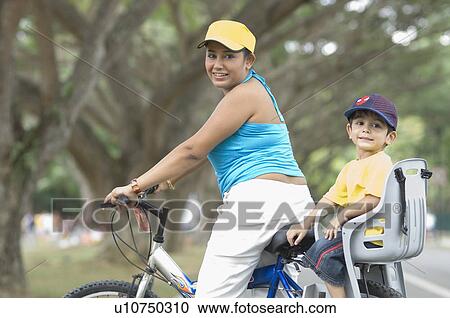 Stock Image - Portrait of a mid adult woman sitting with her son on a bicycle. Fotosearch